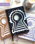 Three decorative Lunar Planners with celestial designs on a white surface with candles and crystals.
