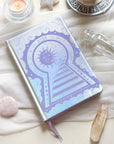 Stunning silver planner decorative 2026 Moon Planners / notebooks with 2026 design on a white surface with candles and crystals. Goddess Provisions Planner - Exclusive