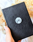 Mystical Musings Divination Diary with black vegan leather cover, featuring embossed clear quartz crystal and moon phases design. A celestial journal for dreams and manifestations. Available at Goddess Provisions.