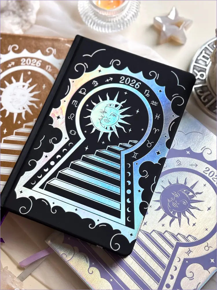 Stunning black planner decorative 2026 Moon Planners / notebooks with 2026 design on a white surface with candles and crystals. Goddess Provisions Planner - Exclusive. With champaign 2026 planner and Silver 2026 planner in the background. 
