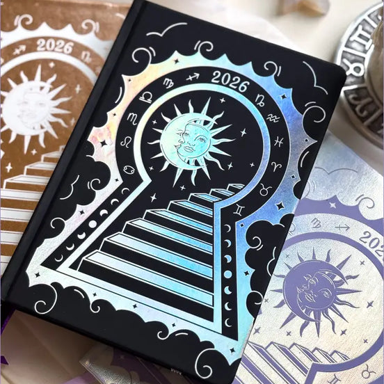Stunning black planner decorative 2026 Moon Planners / notebooks with 2026 design on a white surface with candles and crystals. Goddess Provisions Planner - Exclusive. With champaign 2026 planner and Silver 2026 planner in the background. 