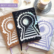 Three decorative Lunar Planners with celestial designs on a white surface with candles and crystals.