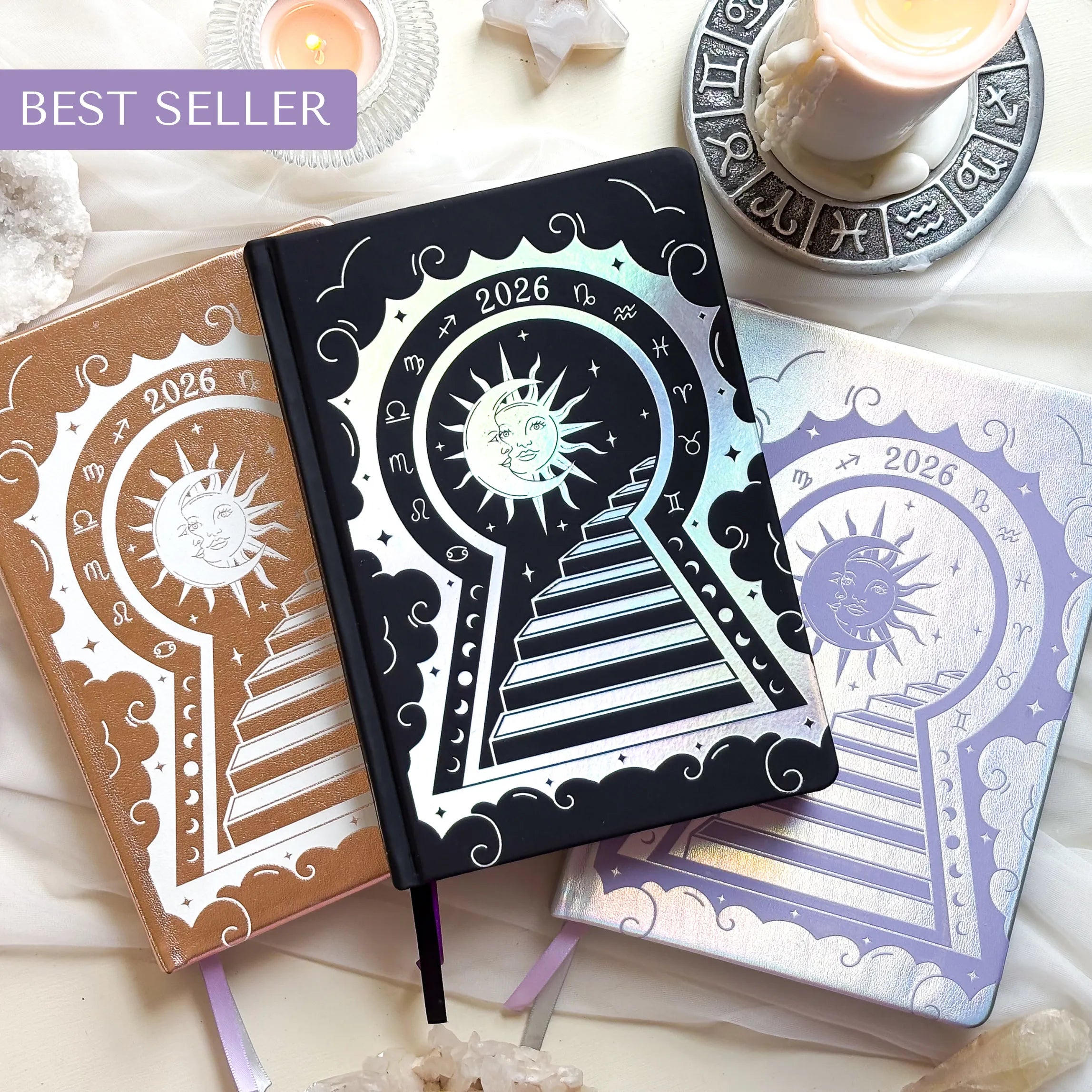 Three decorative Lunar Planners with celestial designs on a white surface with candles and crystals.