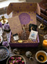 April subscription women box featuring crystal ritual set with tea, notebook, spoon, facial steam, broom, and amethyst crystal