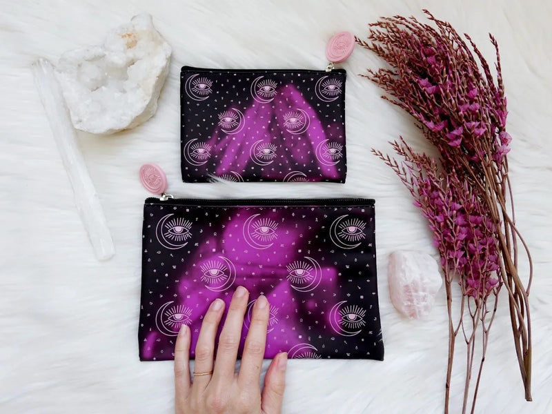 Purple alchemy-inspired pouch changing to bright magenta when touched, featuring mystical symbols and zipper closure.
