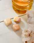Three tumbled stones and a crystal cluster on a light surface with a glass container of honey in the background.