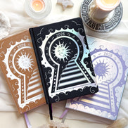 Three decorative 2026 Moon Planners / notebooks with 2026 design on a white surface with candles and crystals. 