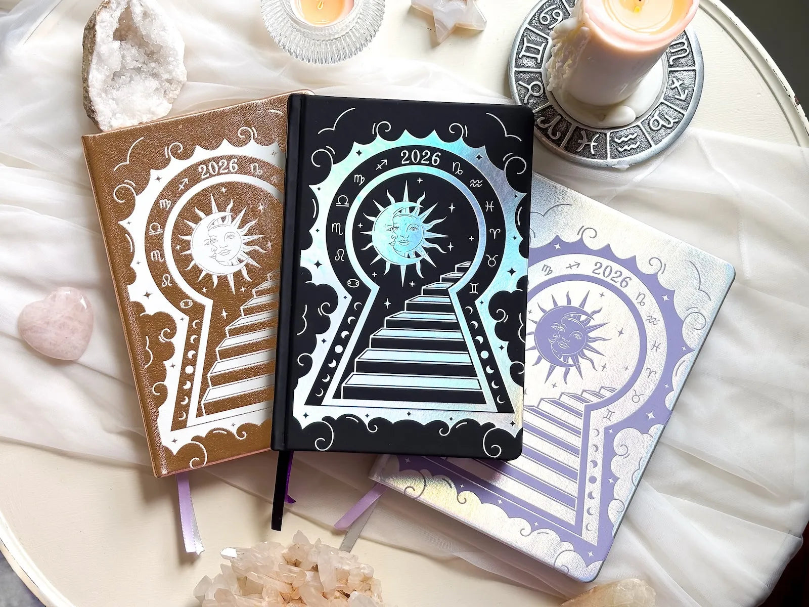 Three decorative 2026 Moon Planners / notebooks with 2026 design on a white surface with candles and crystals. 