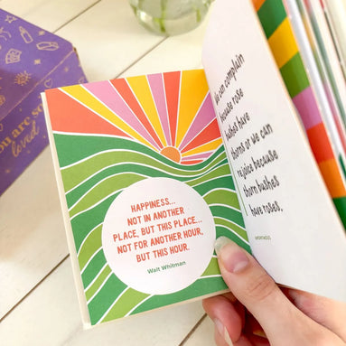 Pocket-sized wellness book with bright cover colors and positive affirmations inside.