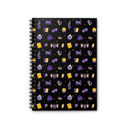 A spiral-bound journal with a black cover featuring a whimsical witch design with various symbols and shapes in purple, gold, and white colors.