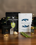 Glowing crystal, 'Money Magick' package, 'Manifest' book, and other mystical items on a wooden surface.
