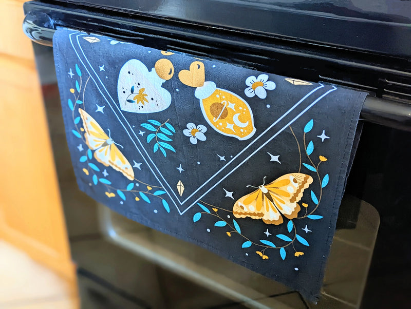 Mystic Nights tea towel with celestial artwork hanging in a cozy kitchen space.