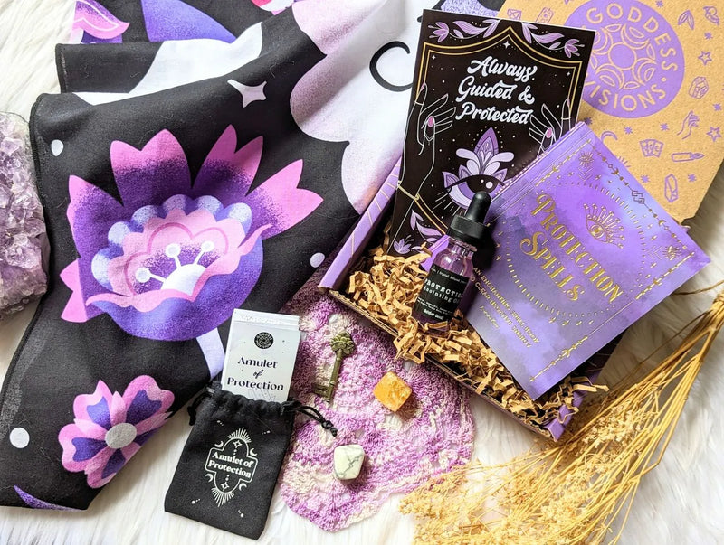 Flat lay of the Protection Box items including altar cloth, amulet, crystals, and anointing oil on a celestial background.