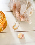 Gold necklace with a sun design on a white surface with crystals and a candle.