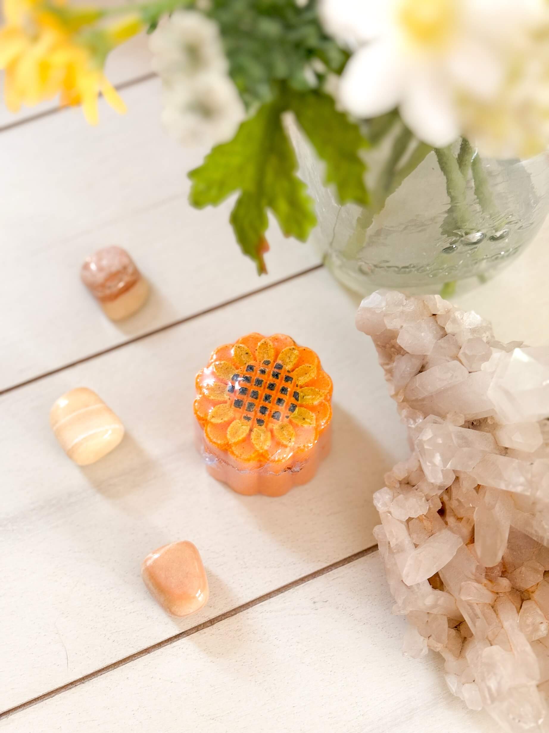 Decorative orange stone with crystals and flowers on a wooden surface