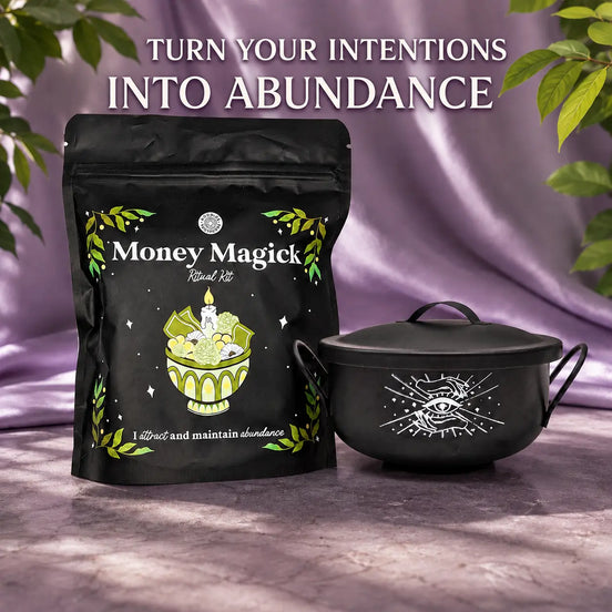 A black stand-up pouch labeled 'Money Magick Ritual Kit' stands beside a matching black cauldron with a lid, set against draped purple fabric and green leaves. Large text at the top reads 'TURN YOUR INTENTIONS INTO ABUNDANCE.