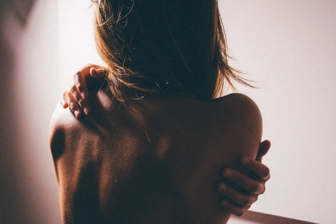 Bare-shouldered person with clasped hands around arms in article about hormones