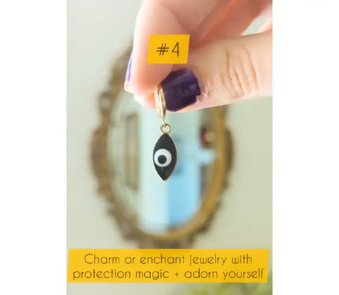 Black evil eye charm with gold hoop held by fingers with purple nail polish