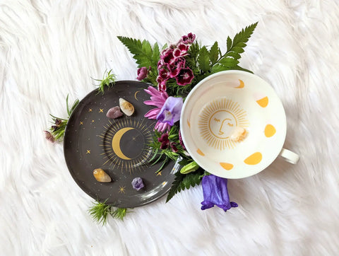 Black saucer with gold crescent moon and stars paired with white teacup featuring gold sun face and yellow moon shapes for Divination Practices article