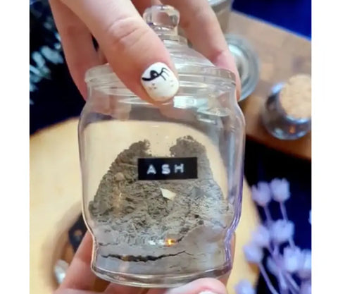 Glass jar filled with gray ash used in making black salt for culinary and spiritual uses