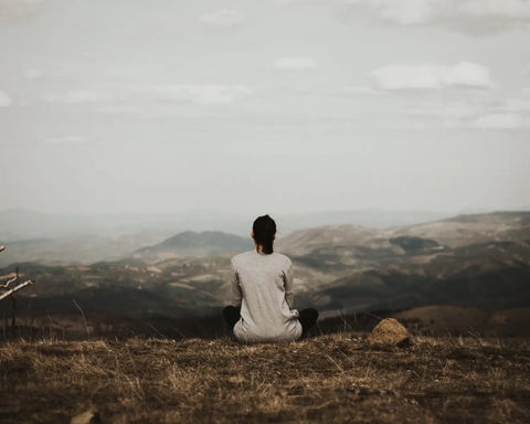 Person in a light-colored shirt sitting on a grassy hill during evening ritual for energy restoration