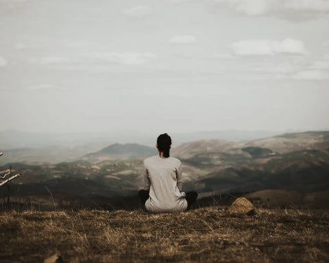 Person sitting on a hilltop overlooking a valley for Throat Chakra Activation article