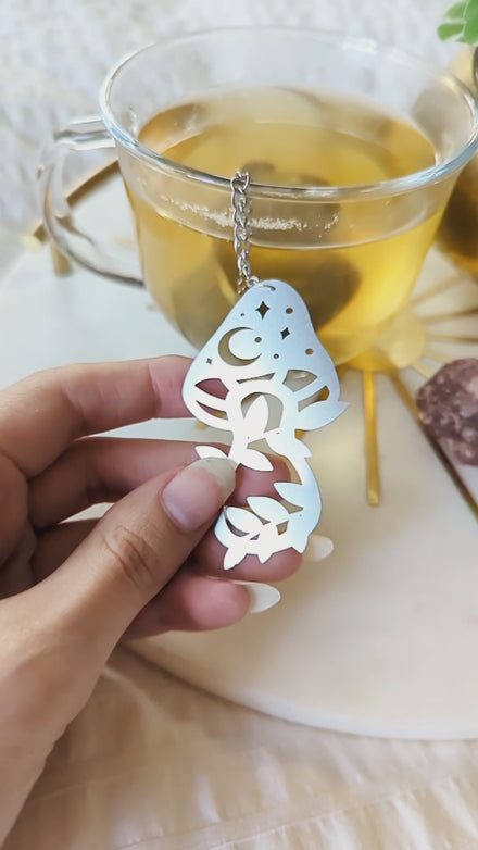 Video showcasing the Herbal Alchemy tea infuser steeping loose leaf tea in a mug while highlighting the mushroom charm and mystical design details.