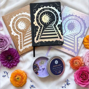 Three 2026 moon planners or 2026 Lunar planners with a spring Haze candle with herbs inside and flowers on a light cream silk surface