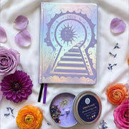 Three Silver 2026 moon planners or 2026 Lunar planners with a purple spring Haze candle with herbs inside and flowers on a light cream silk surface