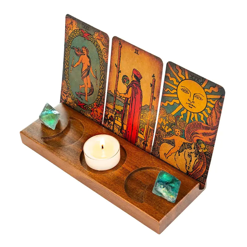 A wooden tarot card stand with three upright tarot cards, a small white tea light candle, and two green crystal balls on a clean white background.