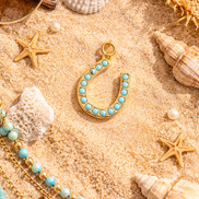 Turquoise horseshoe charm jewelry on beach themed flat lay with sand and ocean inspired styling.