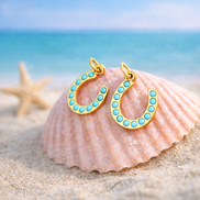 Gold turquoise horseshoe charm displayed in beach themed flat lay styling.