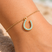 Turquoise horseshoe charm held in hand showing gold charm jewelry detail.