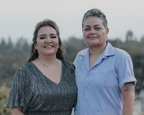 Two smiling women, one in a dark patterned dress and the other in a light blue shirt, connecting with ancestors and intuition