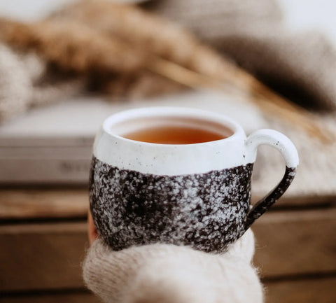 Two-toned ceramic mug with speckled black bottom and white top filled with a warm beverage
