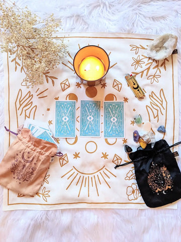 White cloth with gold mystical symbols, blue tarot cards, candle, scroll, crystals for Winter Solstice Ritual