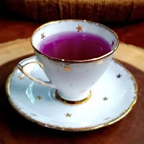 White teacup and saucer with gold trim and star patterns holding a purple beverage
