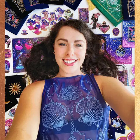Young woman with dark curly hair smiling in a sheer blue seashell and chain top