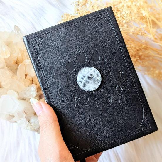 Mystical Musings Divination Diary with black vegan leather cover, featuring embossed clear quartz crystal and moon phases design. A celestial journal for dreams and manifestations. Available at Goddess Provisions.