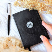 A5 celestial journal made from recycled paper, with 120 lined pages and embossed moon phases design on black vegan leather. Perfect for magical moments and daily to-dos.